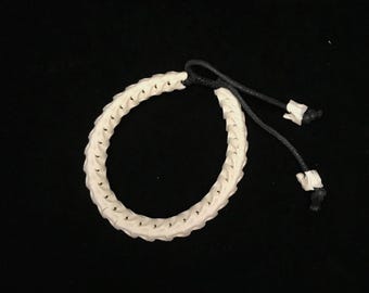 May include: White bone bracelet with a black cord and adjustable closure. The bracelet is made of small, interlocking pieces of bone.