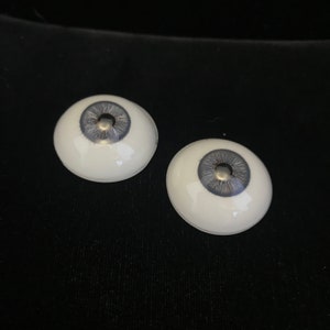 May include: Two white doll eyes with a gray iris and a silver pupil.
