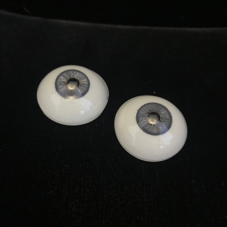 May include: Two white doll eyes with a gray iris and a silver pupil.