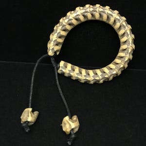 Könnte beinhalten: Ein einzigartiges Armband aus Knochensegmenten, das ein kreisförmiges Design mit einer schwarzen Kordel und Knochenanhängern aufweist. Das Armband hat eine natürliche, cremefarbene und beige Farbgebung, vor einem dunklen Hintergrund.