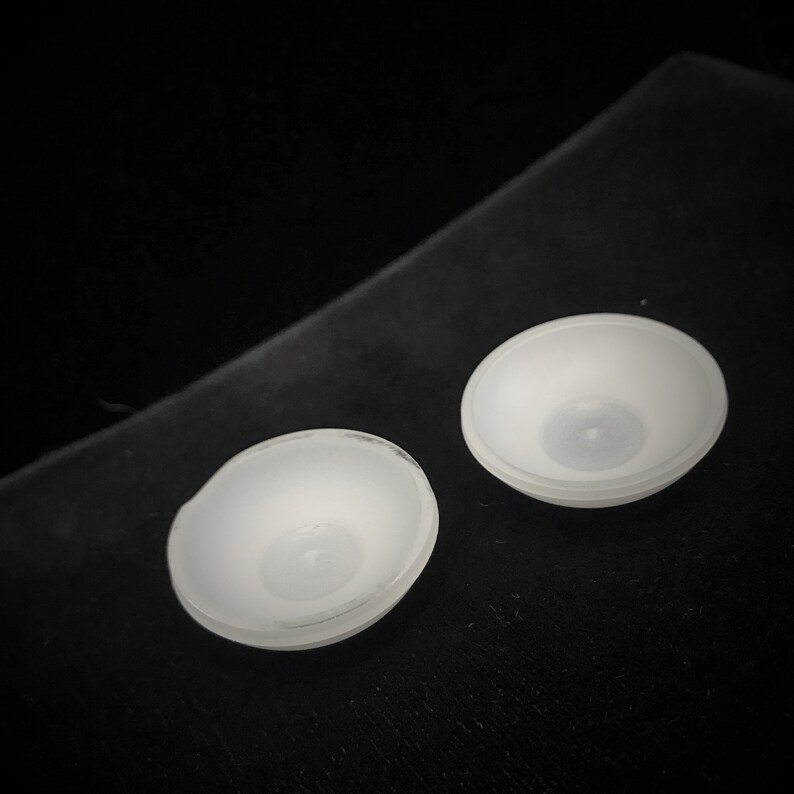 May include: Two white ceramic bowls with a smooth, rounded surface. The bowls are slightly concave and have a small, circular indentation in the center.