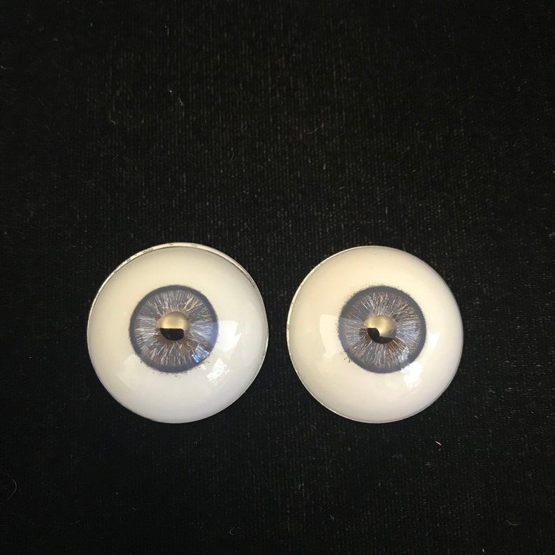 May include: Two white doll eyes with a blue iris and a gold pupil.