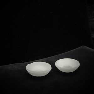 May include: Two white ceramic bowls on a black surface. The bowls are round and have a smooth, glossy finish.