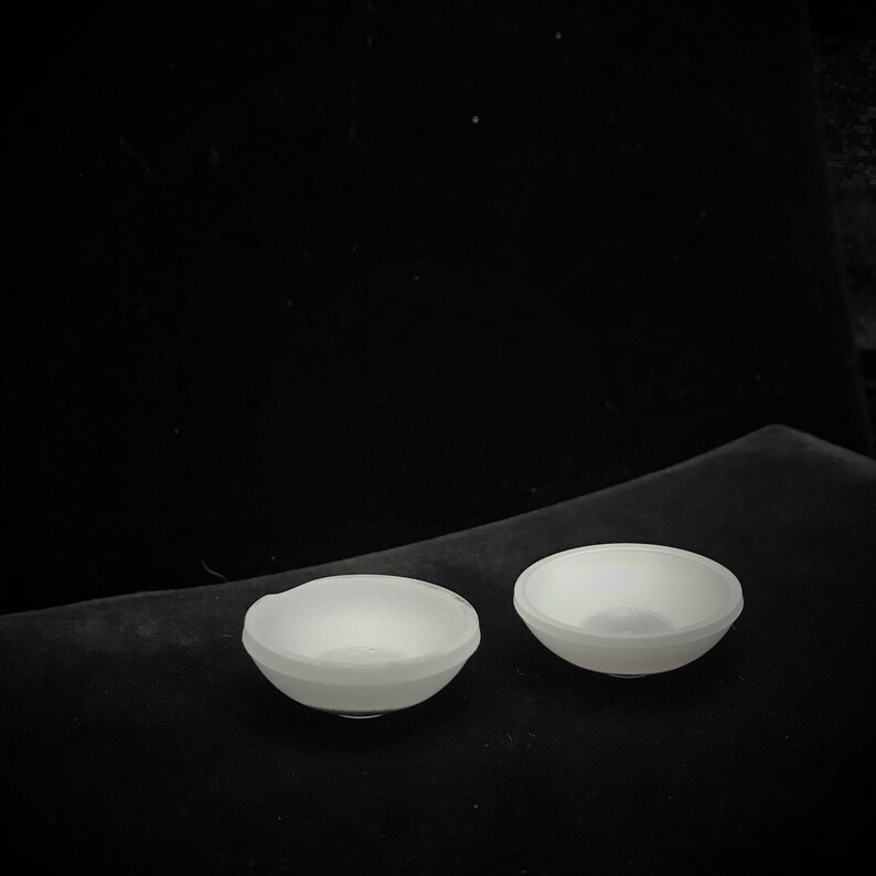 May include: Two white ceramic bowls on a black surface. The bowls are round and have a smooth, glossy finish.