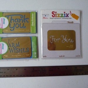 May include: Four craft items are displayed: two green and gold "Thank You" and "Warm Wishes" cards, an embossing folder with "For You" text, and a ruler. The cards have blue text and are from Ellison Design. The Sizzix embossing folder is in a clear plastic package.