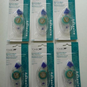May include: Six Tombow permanent adhesive tape runner refills in their original packaging. Each refill is in a clear plastic case with a blue cap and a teal and yellow tape roll. The packaging is teal and white.
