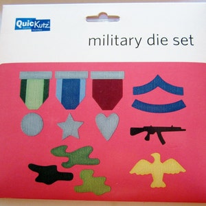 May include: A pink card with a military die set. The set includes paper cutouts of medals, a star, a heart, chevrons, a rifle, an eagle, and camouflage shapes. The words "military die set" are printed on the card.