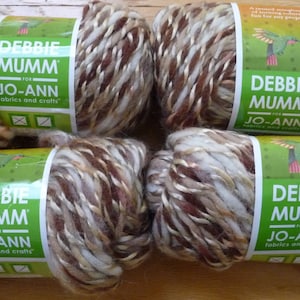 May include: Four skeins of Debbie Mumm yarn for Jo-Ann fabrics and crafts. The yarn is a mix of brown, cream, and tan colors. Each skein has a green label with the Debbie Mumm logo and a hummingbird illustration.