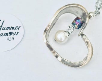 May include: A silver heart-shaped pendant necklace with a pearl and iridescent bead accent. The pendant hangs from a delicate chain. The necklace is on a white background.