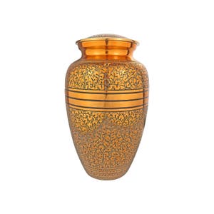 Könnte beinhalten: Eine goldene Metallurne mit floralem Design. Die Urne hat eine breite Öffnung und einen schmalen Boden.