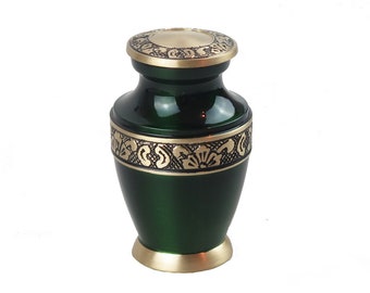 Puede incluir: Una pequeña urna de metal verde con tapa y ribetes dorados. La urna tiene un diseño floral alrededor del medio.
