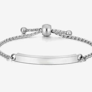 May include: A silver bracelet with a chain and a sliding bead. The bracelet has a flat, rectangular tag that can be engraved.