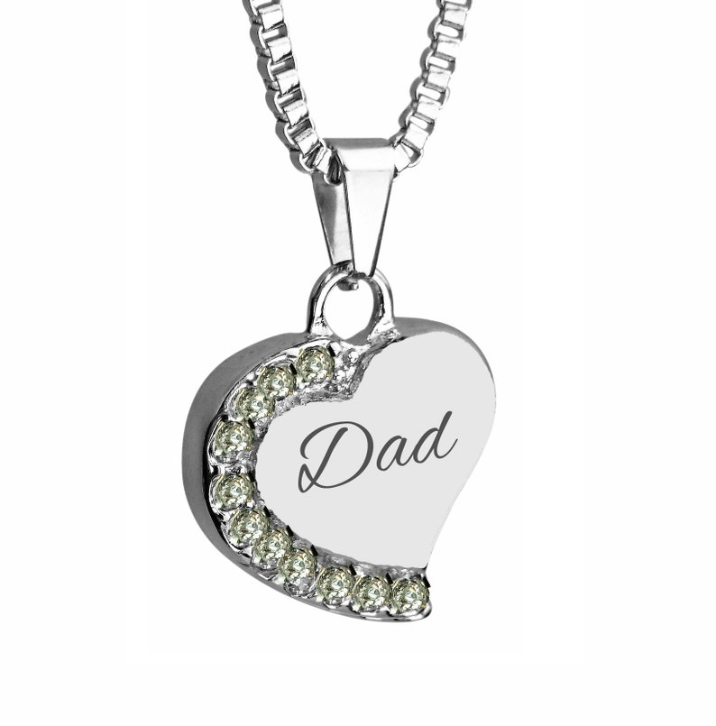May include: Silver heart-shaped pendant necklace with a clear crystal trim and the word "Dad" engraved on the front.