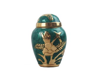 Puede incluir: Una pequeña urna verde y dorada con un diseño floral. La urna tiene una tapa y está hecha de metal.