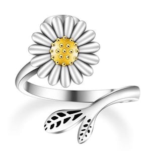 May include: A silver ring featuring a white daisy flower with a gold centre. The ring has a delicate stem with two leaves.