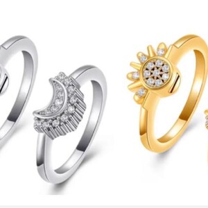 May include: Two silver-toned rings and two gold-toned rings. Each set features one ring with a circular sun motif and one ring with a crescent moon motif. All four rings are embellished with small, clear, sparkling stones set into the metal.