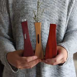 May include: Three wooden vases in different colors and styles. The vases are made of wood and have a natural finish. The vases are all different sizes and shapes. The vases are perfect for displaying flowers or other decorative items.
