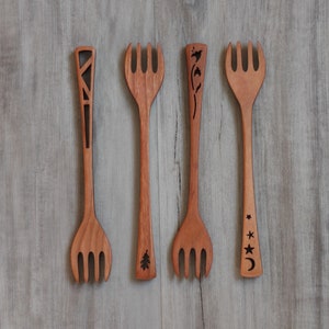 May include: Four wooden forks with different designs carved into the handles. The forks are arranged in a row on a light gray wooden surface.