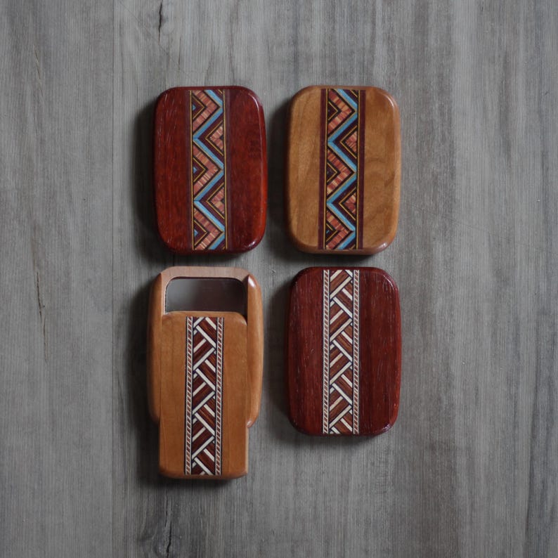 May include: Four wooden coasters with geometric inlay designs. Two coasters are rectangular with a dark reddish-brown finish, and two are lighter brown. The inlay features zig-zag patterns in shades of blue, white, and brown.