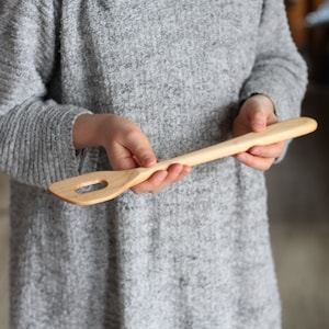 May include: A wooden spatula with a hole in the handle. The spatula is light brown and has a smooth finish.