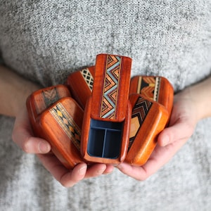 May include: A set of small wooden boxes with intricate geometric patterns in shades of brown, red, and blue. The boxes are open and reveal a blue interior.