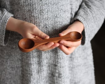 May include: A wooden measuring spoon with two different sized scoops. The spoon is made of natural wood and has a smooth finish.