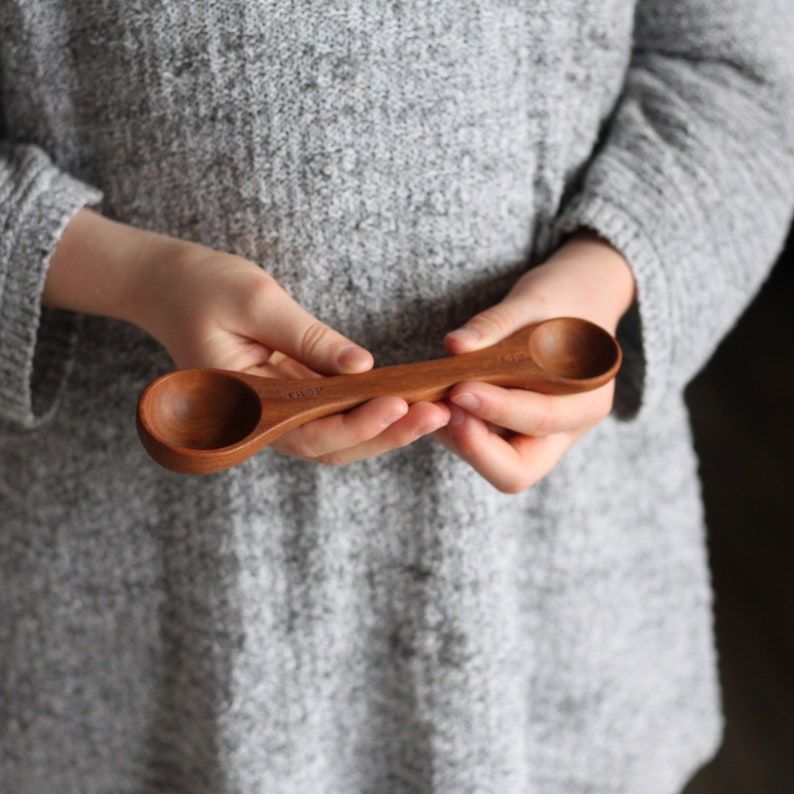 May include: A wooden measuring spoon with two different sized scoops. The spoon is made of natural wood and has a smooth finish.