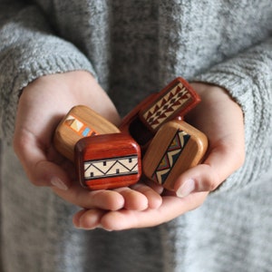 May include: Four small, rectangular wooden boxes with rounded edges, each featuring unique inlaid geometric patterns in various colors including red, blue, yellow, and black. The boxes are crafted from different wood tones and display intricate designs.