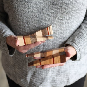 Puede incluir: Tres topes de puerta de madera hechos de diferentes tipos de madera. Los topes de puerta tienen forma de cu&ntilde;a y tienen un patr&oacute;n de rayas rojas, blancas y marrones.