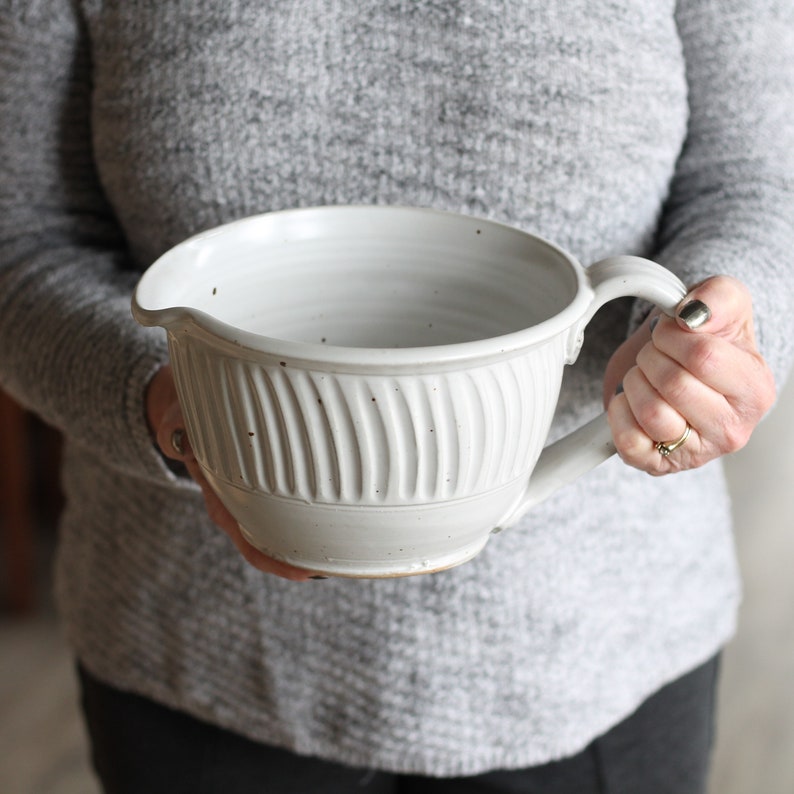 May include: A white ceramic mixing bowl with a large handle. The bowl has a textured, ribbed design.