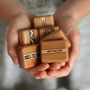 May include: A collection of small, rectangular wooden blocks with smooth, polished surfaces. Each block features a central inlay strip decorated with colorful geometric patterns, including diamonds, chevrons, and lines in red, green, and blue tones.