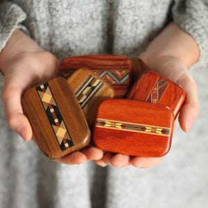 May include: A collection of small, rectangular wooden boxes with rounded corners, featuring intricate inlaid geometric patterns in various wood tones including light, medium, and dark brown, with some accents in orange and blue hues.