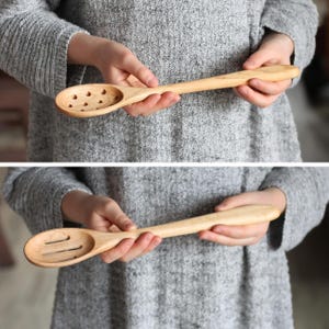 May include: A light-colored wooden spoon with a perforated bowl featuring multiple circular holes, shown in the top image, and a second wooden spoon with a bowl featuring three elongated, parallel slots, shown in the bottom image.