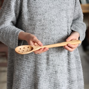 May include: A wooden spoon with holes in the bowl, perfect for scooping and draining food. The spoon is made of natural wood and has a long handle.