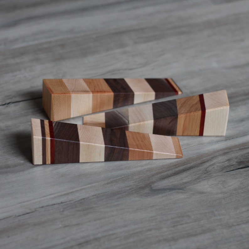 Puede incluir: Tres topes de puerta de madera con un patr&oacute;n rayado de madera clara y oscura. Los topes de puerta est&aacute;n dispuestos en forma triangular.
