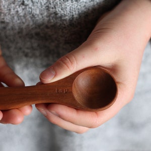 May include: A wooden spoon with the word "tsp" engraved on the handle. The spoon is held in a person's hand.
