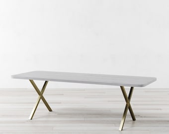 May include: A white rectangular dining table with a gold metal X-shaped base. The table is on a light wood floor.