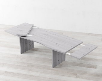 May include: A white wooden dining table with two leaf extensions. The table has a slightly curved top and is supported by four legs.