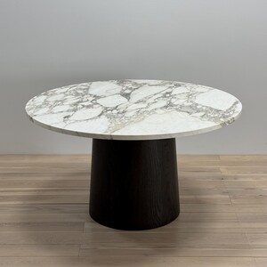 May include: A round marble table with a black wood base. The table top has a white and grey marbled pattern.