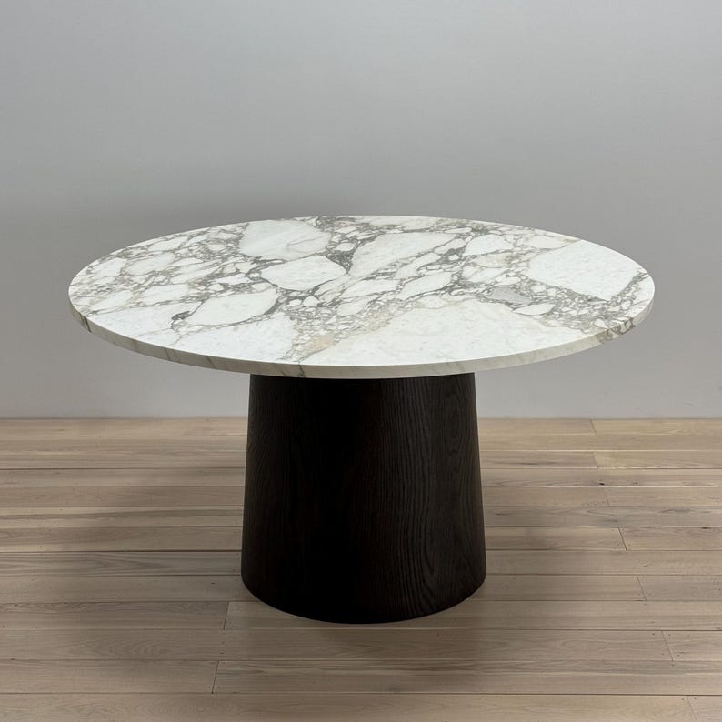 May include: A round marble table with a black wood base. The table top has a white and grey marbled pattern.