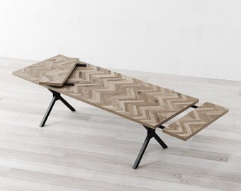 May include: A wooden dining table with a chevron pattern top and black metal legs. The table has two leaves that can be extended to increase the table's length.