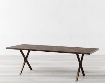 May include: A long, rectangular wooden dining table with a chevron pattern on the top. The table has a brass X-shaped base.