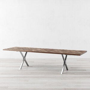 May include: A long, rectangular wooden dining table with a chevron pattern top and a silver metal base with two X-shaped supports.