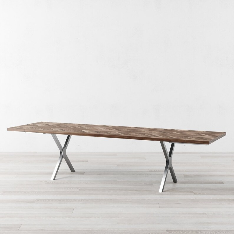 May include: A long, rectangular wooden dining table with a chevron pattern top and a silver metal base with two X-shaped supports.