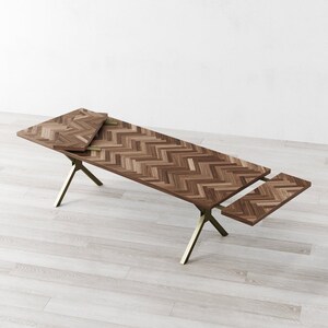 May include: A wooden dining table with a chevron pattern top and gold metal legs. The table has two leaves that can be extended to increase the table's length.
