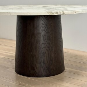 May include: A round, white marble table top with a dark brown wood base. The base is a cylinder shape with a slightly flared bottom.