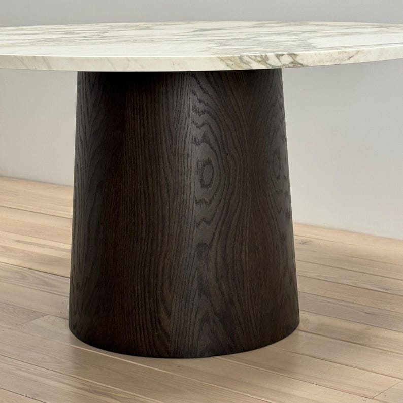 May include: A round, white marble table top with a dark brown wood base. The base is a cylinder shape with a slightly flared bottom.