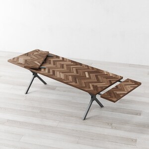 May include: A wooden dining table with a chevron pattern top and a black metal base. The table has two leaves that can be extended to increase the table's length.