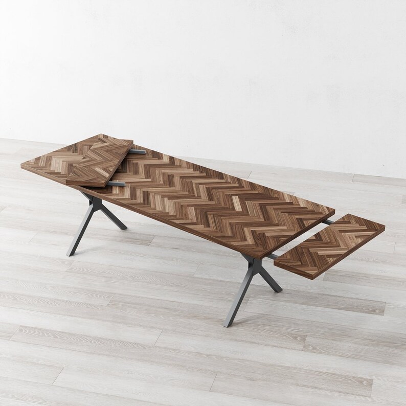 May include: A wooden dining table with a chevron pattern top and a black metal base. The table has two leaves that can be extended to increase the table's length.
