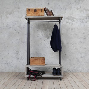 May include: A gray wooden coat rack with black metal pipes. The rack has a top shelf, a hanging rod, and a lower shelf. A wooden box, a stack of books, a jacket, and a pair of shoes are on the rack.